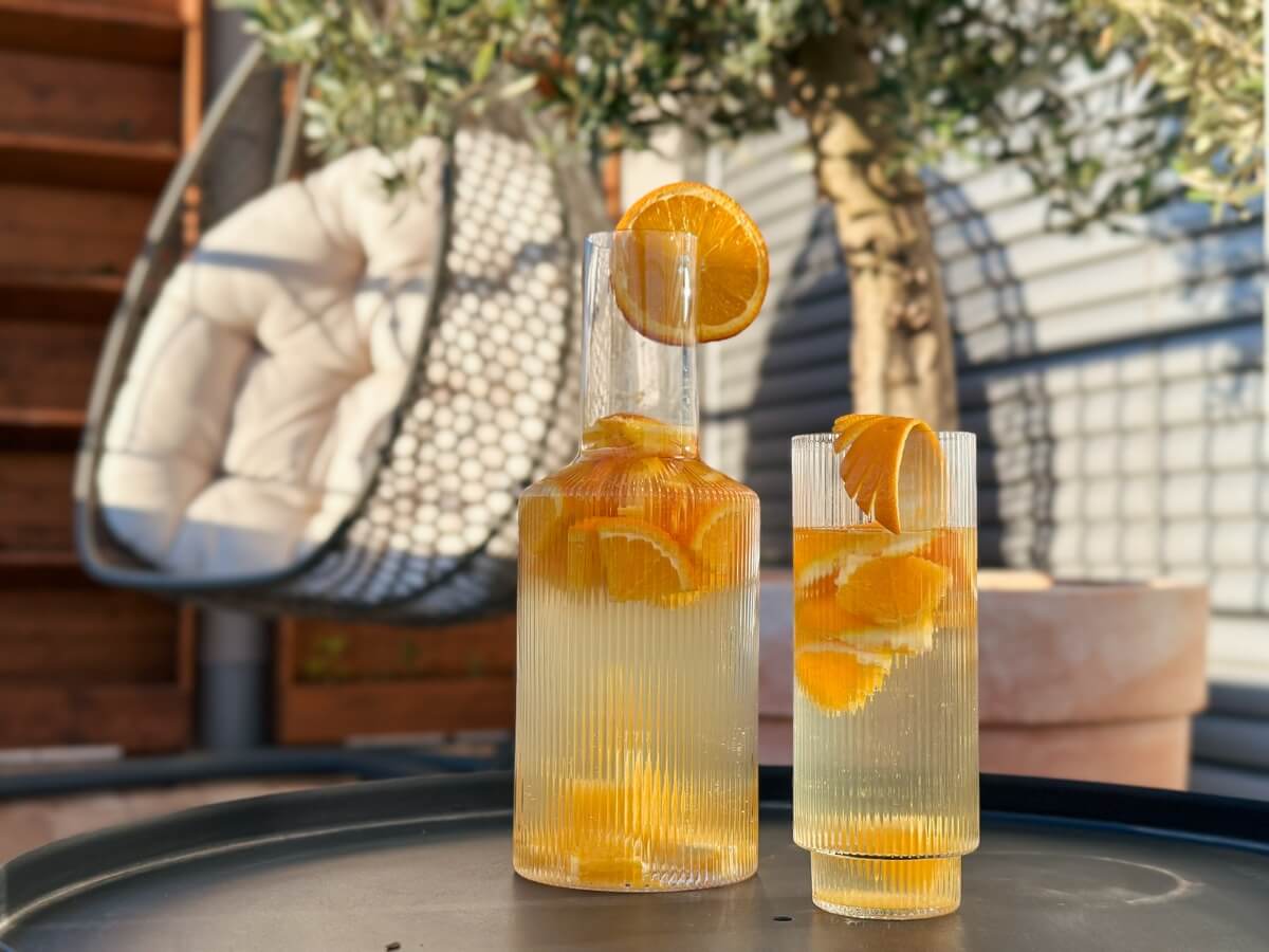 Citrusová limonáda s kúskami pomaranču naliata v dizajnovej karafe a pohári.