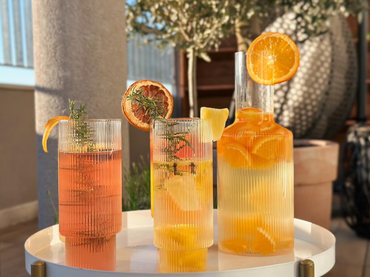 Sklenená karafa s citrusovou limonádou a rôznofarebné limonády vo vysokých pohároch.