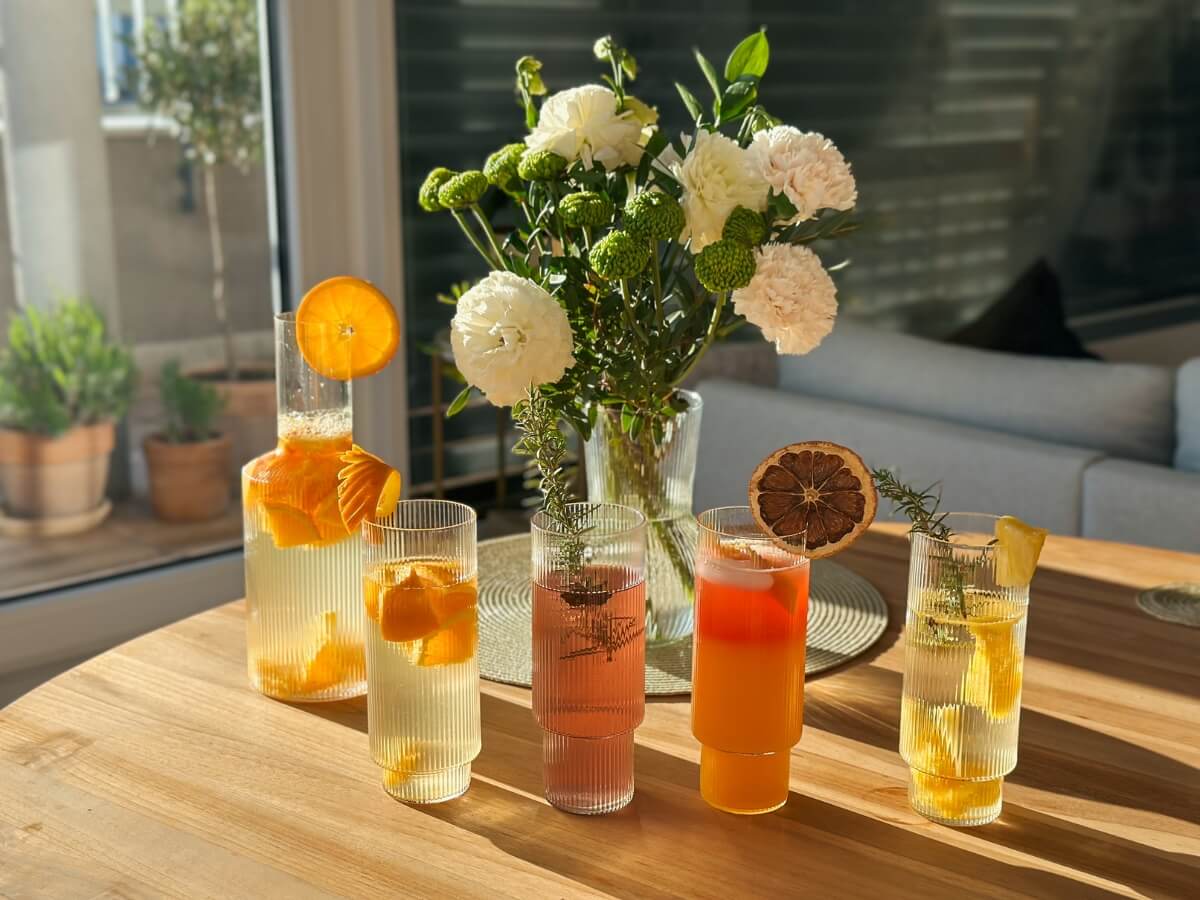 Limonády v sklenených vrúbkovaných pohároch a karafe s rôznymi ovocnými ozdobami.