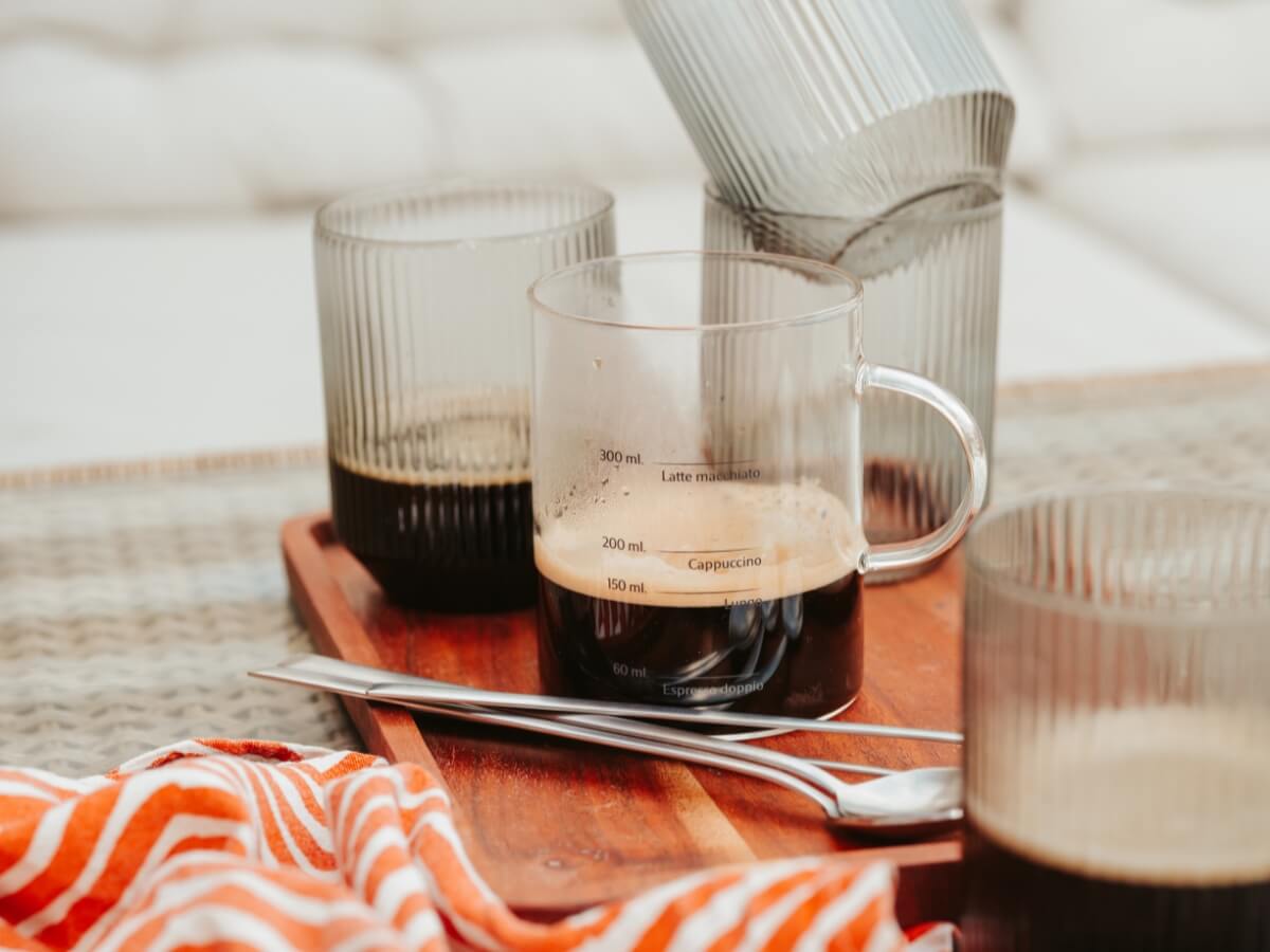 Sklenená odmerka kávy a káva naliata v sklenených vrúbkovaných pohároch.
