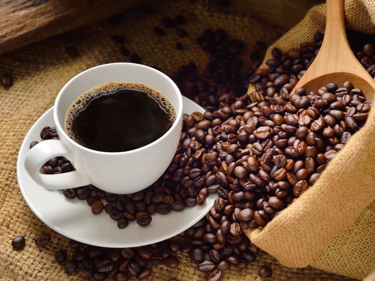 Klasická zalievaná káva v bielej šálke obsypaná kávovými zrnami.