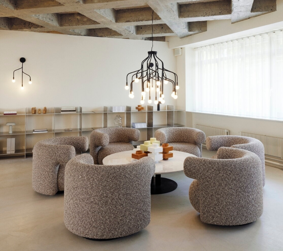 Závesné čierne svietidlo v rozvetvenom dizajne nad kruhovým sedením v hale.