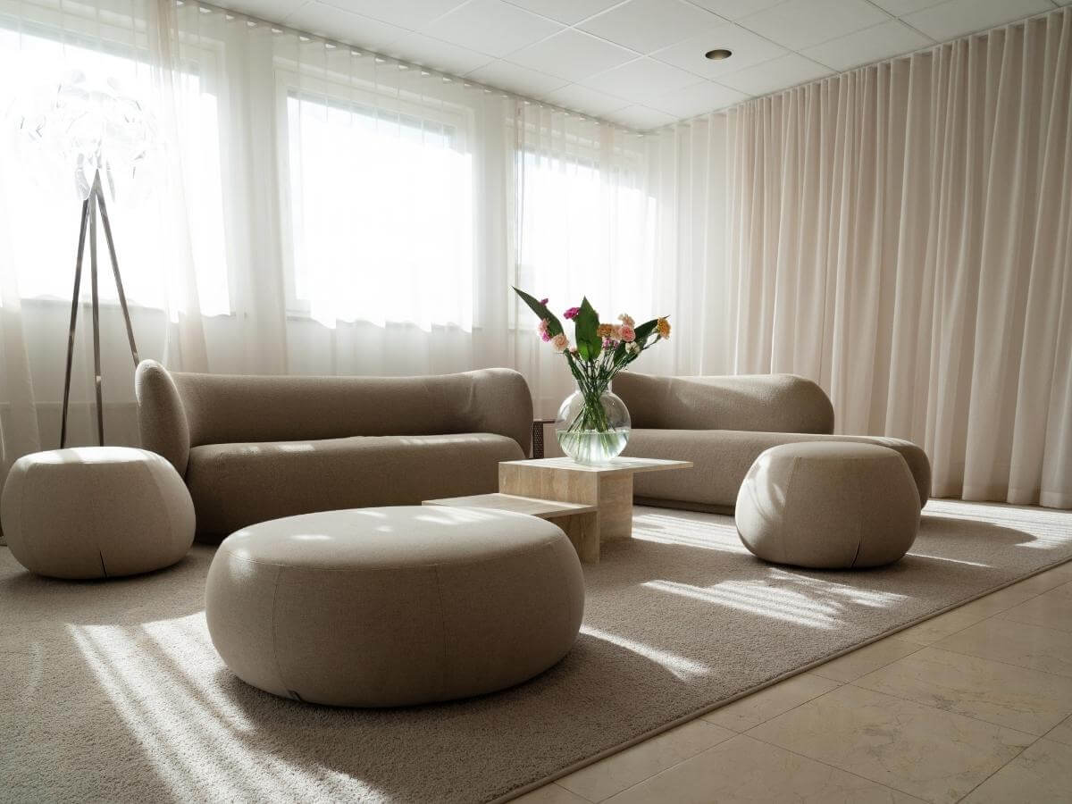Minimalisticky zariadená obývačka v prírodných farbách s veľkou vázou s kvetmi na konferenčnom stolíku.
