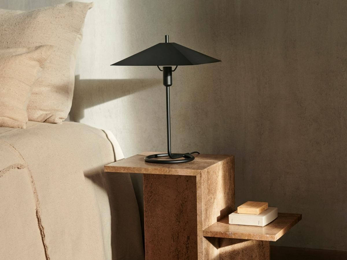 Kamenný dizajnový nočný stolík s čiernou minimalistickou lampou.