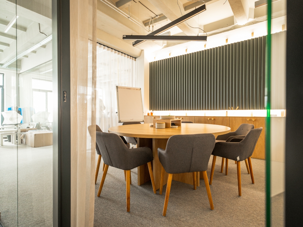 Moderná zasadačka v coworkingu s okrúhlym dreveným stolom a sivými kreslami.