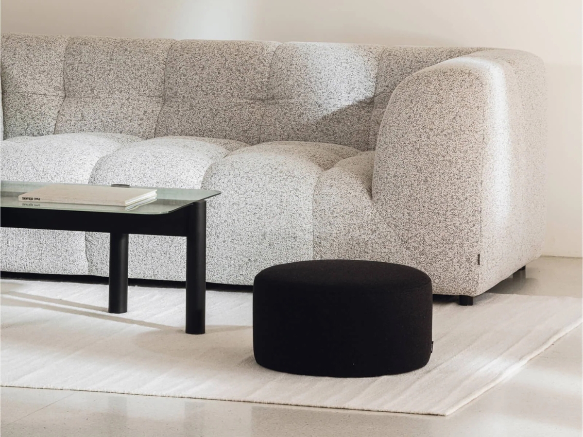 Nízky minimalistický puf v čiernej fabre a s okrúhlym tvarom v obývačke.
