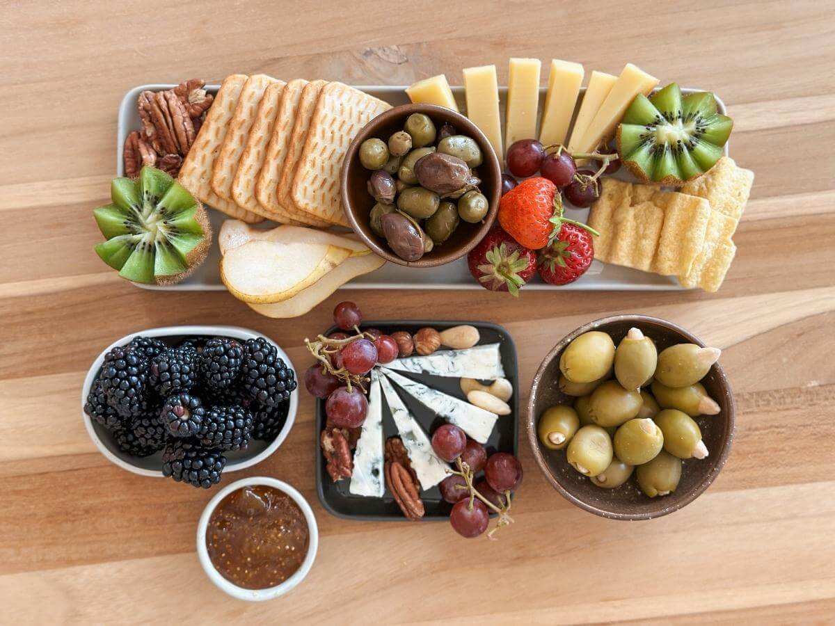 Syry, olivy, ovocie, orechy a krekry uložené na rôznych servírovacích nádobách.