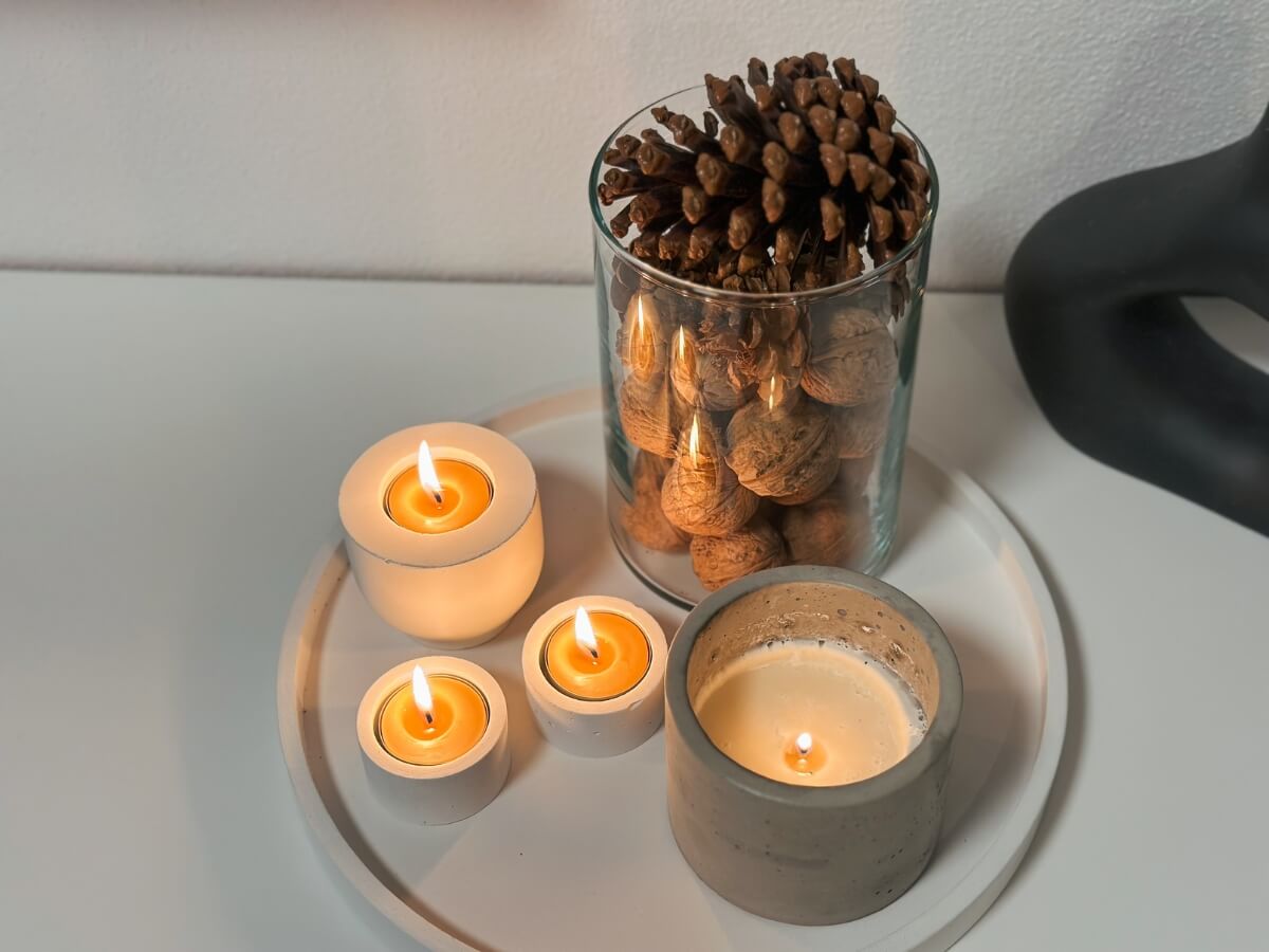 Rôzne veľkosti sviečok v betónových svietnikoch na podnose s jesennou výzdobou šišiek a orechov.