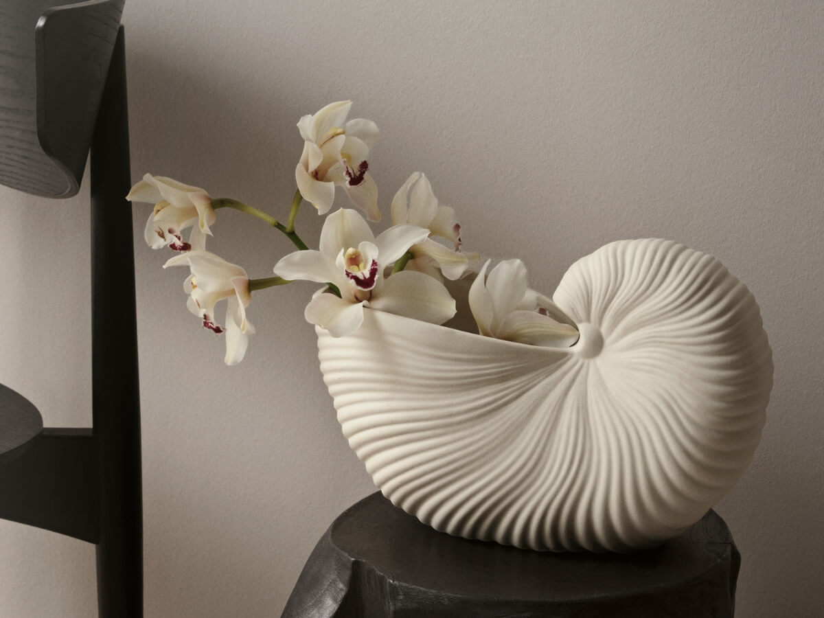 Biela váza v tvare mušle s čerstvými kvetmi.