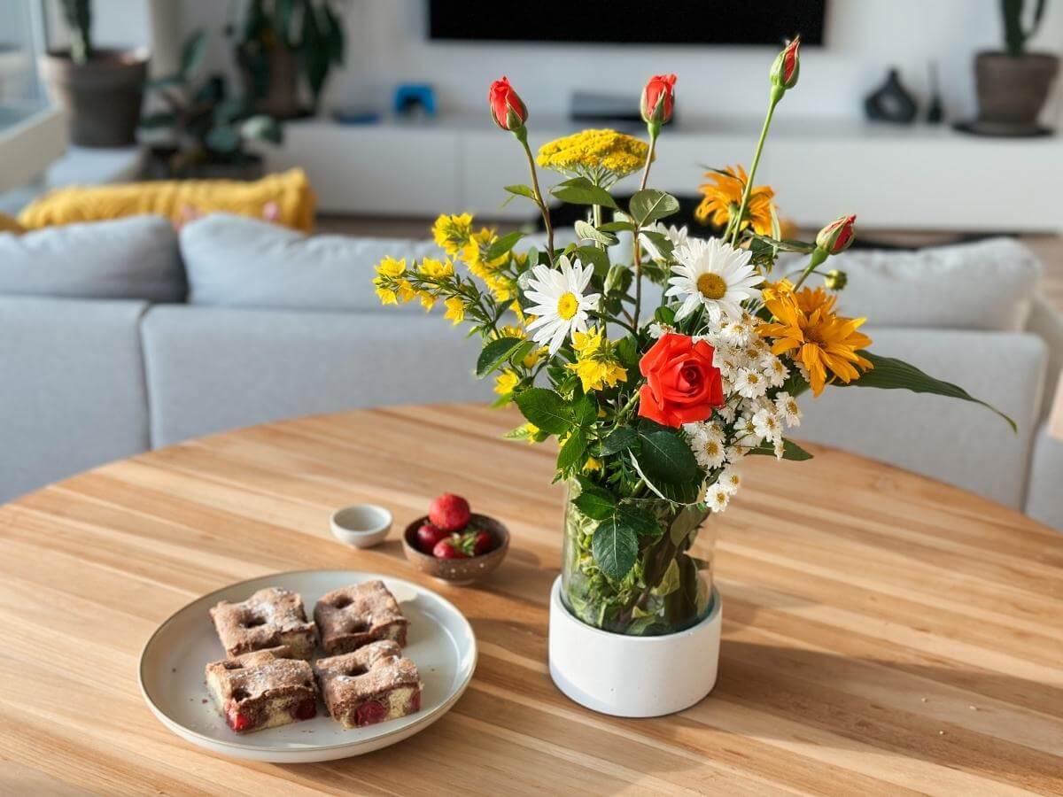 Farebné kvety v dizajnovej váze položené na stole s koláčom.