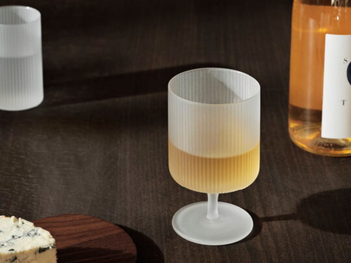 Syr na drevenom podnose, poháre Ripple s vodou a vínom na drevenom stole.