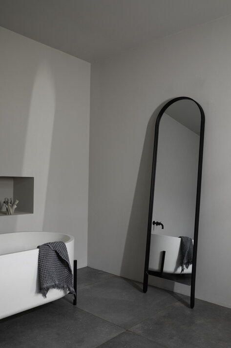 Dizajnové podlahové zrkadlo s rámom z čierneho dubu opreté o stenu v spálni
