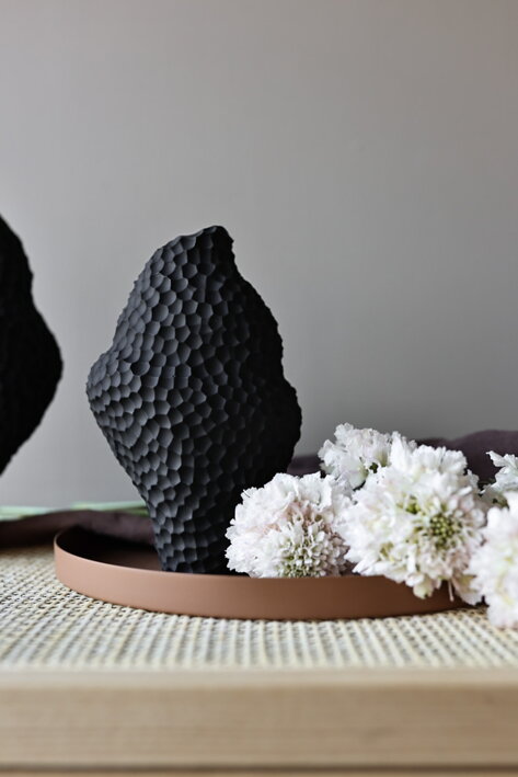 Malá nepravidelná váza z čiernej keramiky na hnedom podnose s bielymi kvetmi