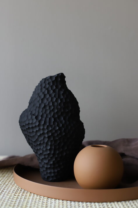 Ručne tvarovaná nepravidelná váza z čiernej keramiky na hnedom podnose