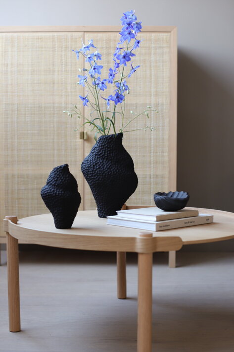 Veľká čierna váza s modrými kvetmi na drevenom stolíku v obývačke