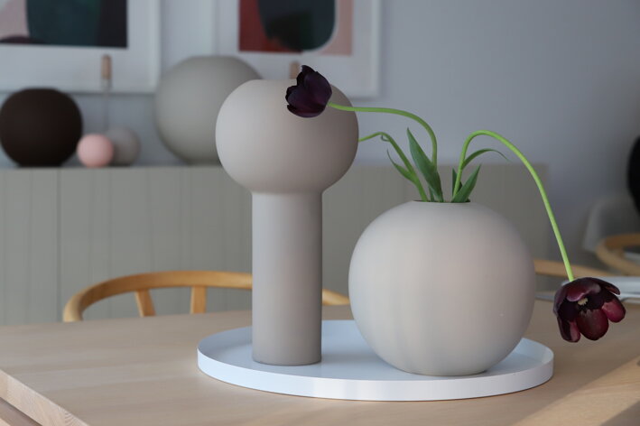 Biely okrúhly podnos z kovu na jedálenskom stole s vázou a svietnikom