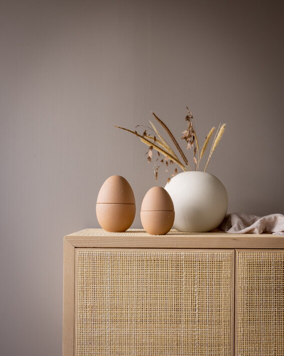 Dekoračné veľkonočné vajíčko z keramiky vo farbe caffe latte na drevenej komode s vázou