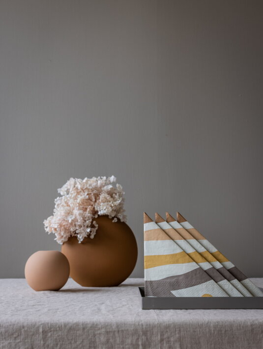 Dizajnové servítky s abstraktnými čiarami v zemitých farbách zložené na stole s vázou