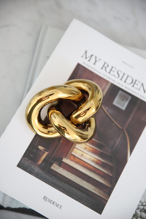 Zlatá keramická dekorácia v tvare malého nekonečného uzla na časopise o dizajne