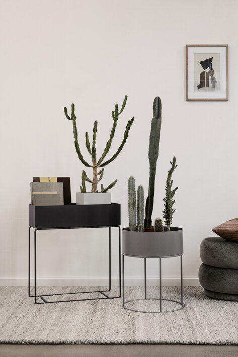 Šedý kovový kvetináč v čiernom dizajnovom stojane v obývačke