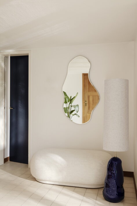 Veľké nepravidelné zrkadlo s mosadzným rámom nad dizajnovou pohovkou v obývačke