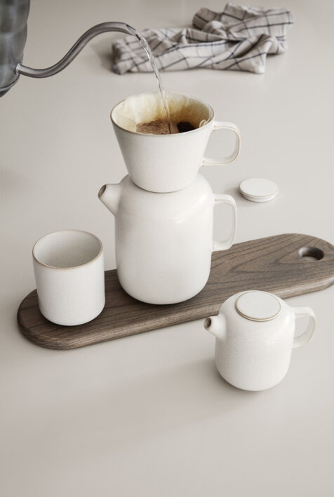 Krémová keramická kanvica na kávu s dripperom na drevenej tácke pri mliekovke