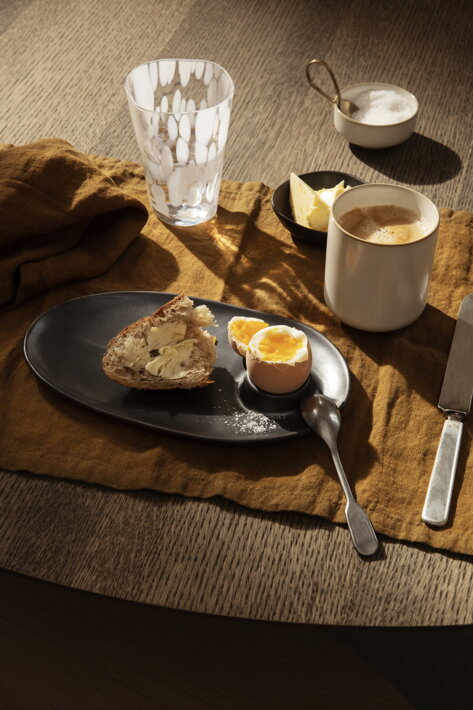 Keramická šálka s kávou na raňajkovom stole s vajíčkom a chlebom