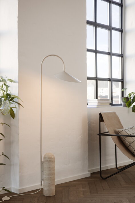 Stojanová lampa z kašmírového kovu a travertínu pri bielej stene nad dizajnovým kreslom