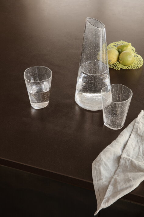 Číra asymetrická karafa na vodu z bublikového skla na stole s citrónmi