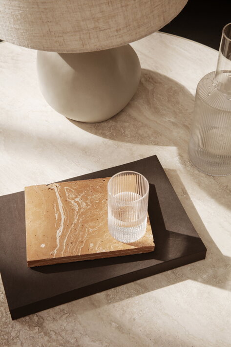 Malý vrúbkovaný pohár s vodou na hlinenej podložke pri stolovej lampe