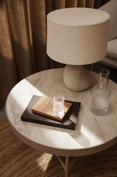 Malý pohárik z vrúbkovaného skla na mramorovom stole pri karafe