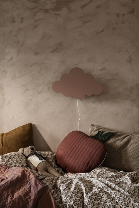 Prešívaný vankúš v tvare jablka pod dizajnovou lampou na posteli v detskej izbe