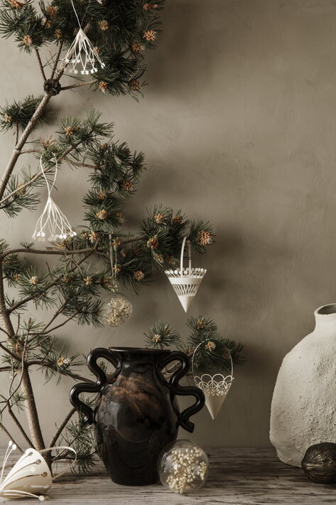 Ozdoby z číreho skla s bielymi sušenými kvetmi na ihličnatej halúzke pri keramickej váze
