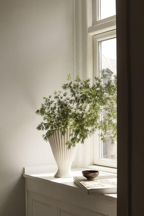 Luxusná biela váza z vrúbkovanej kameniny so živými kvetmi na parapete
