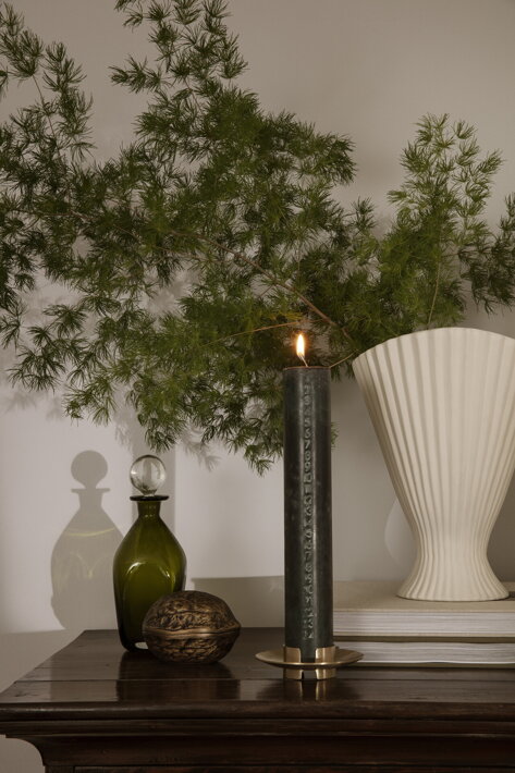 Biela váza z vrúbkovanej kameniny pri adventnej sviečke na komode