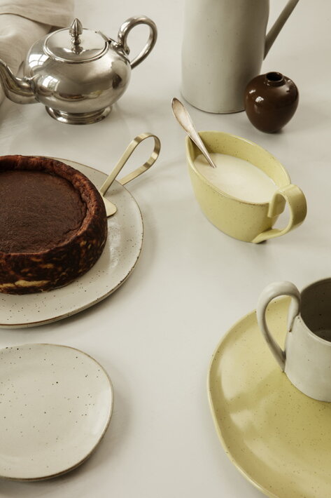 Hnedá miniatúrna váza s glazúrou ako dekoračný predmet na stole s koláčom a keramickým riadom
