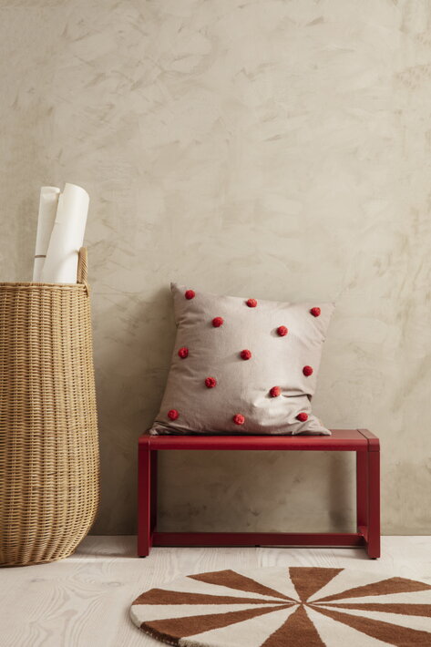 Malý okrúhly koberec v hnedobielej kombinácii pri červenom stolčeku s vankúšom