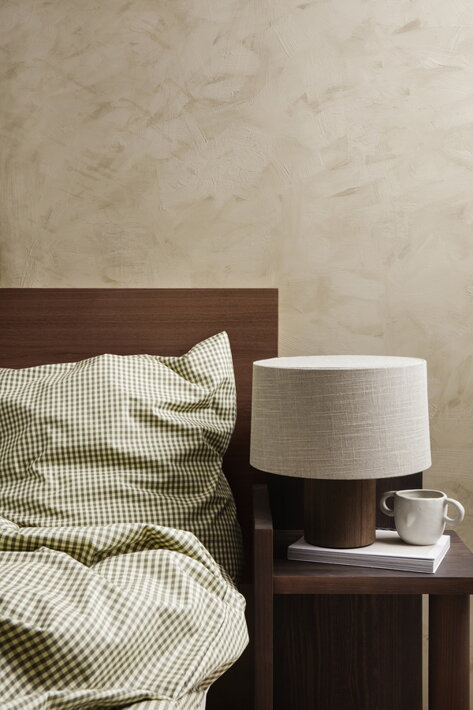 Štýlová stolová lampa s drevenou základňou a textilným tienidlom na nočnom stolíku v spálni