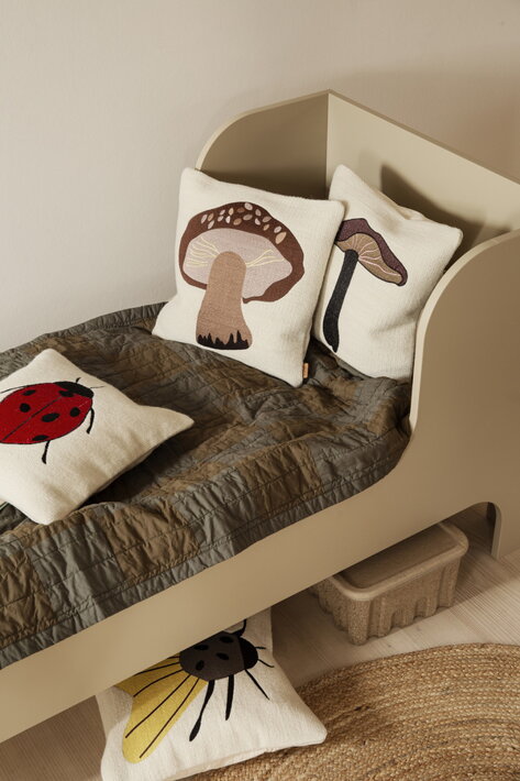 Vankúš z páperia s vlneným návlekom a vyšívaným nočným motýlom na jutovom koberci pod postelou