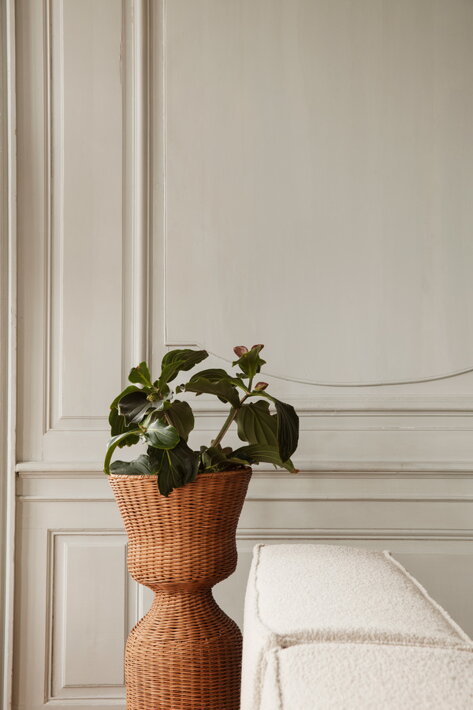 Ručne pletený vysoký stojan na rastliny z prírodného ratanu pri pohovke v obývačke