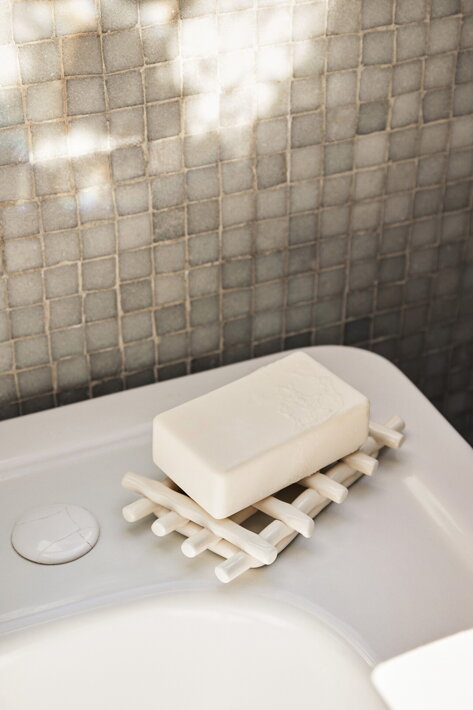 Ručne tvarovaná keramická mydelnička v sivobielej farbe na umývadle v kúpeľni