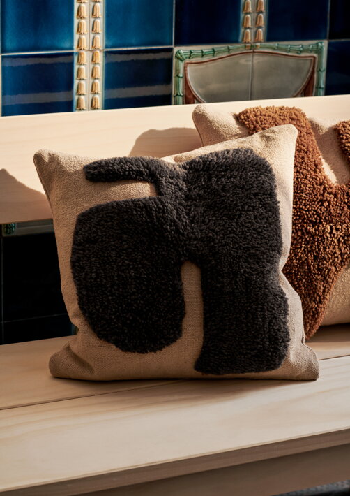 Dizajnový vankúš s ručne všívaným tmavohnedým vzorom na sedačke v obývačke