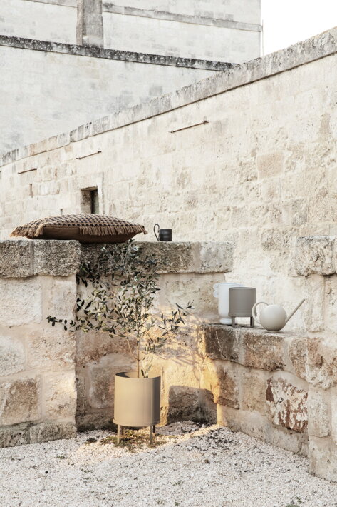 Veľký sivý kvetináč na nožičkách s olivovníkom na kamennej terase