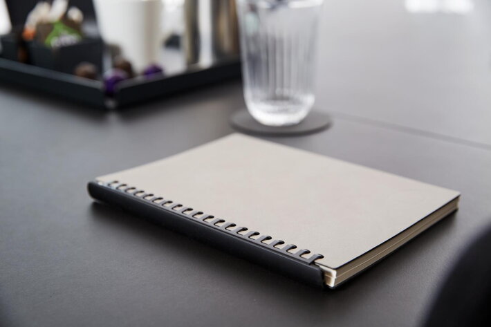 Dizajnový kožený zápisník zo sivej a čiernej kože na stole s pohárom vody