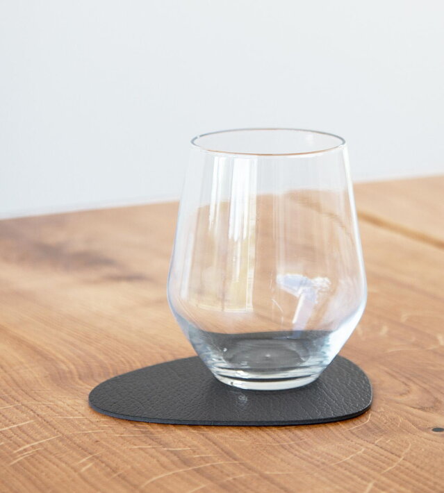 Čierna podložka z recyklovanej kože pod skleneným pohárom na drevenom stole
