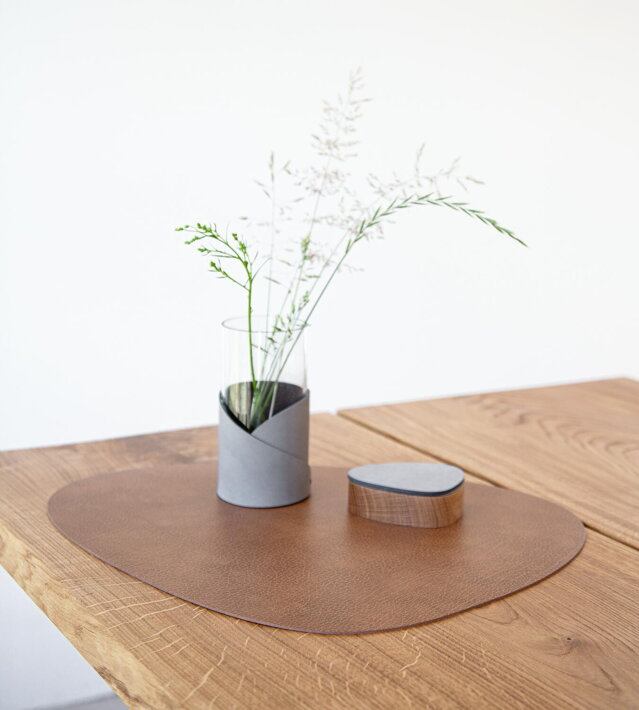 Veľké kožené prestieranie v prírodnej farbe na drevenom stole so soľničkou a dizajnovou vázou