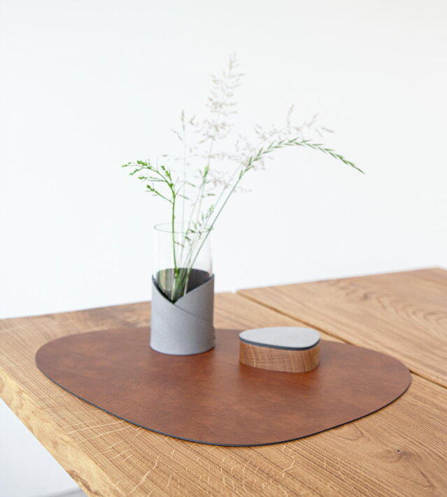 Veľké prestieranie z červenohnedej kože na drevenom stole s dizajnovou vázou a soľničkou