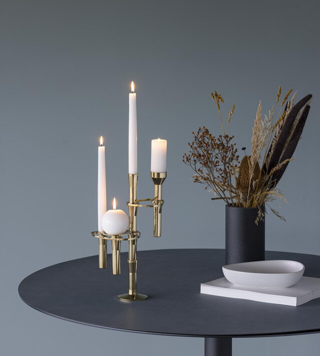 Pozlátený modulárny svietnik zložený z rôznych komponentov s bielymi sviečkami na čiernom koženom stole