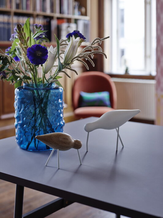 Veľký biely vtáčik z dubového dreva na stole s dizajnovou modrou vázou
