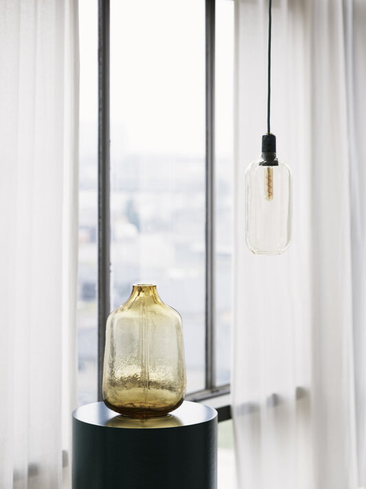 Vysoká dekoračná váza s vrstveným dizajnom z hnedého skla pod štýlovou lampou